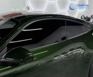 A close-up side view of the same dark green sports car, highlighting the dark window tinting and the reflective quality of the paint under studio lights.